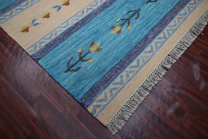 Handwoven kilim rug in blue and beige with tribal geometric motifs and fringe, wool flatweave on dark hardwood.