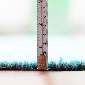 Blue and beige handwoven kilim rug edge in flatweave, with a measuring tape standing upright to show scale.