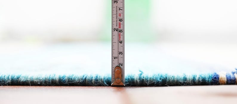 Blue and beige handwoven kilim rug edge in flatweave, with a measuring tape standing upright to show scale.