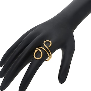 Peut inclure: Une bague dorée enroulée de fil métallique avec un motif tourbillonnant. La bague est faite d'une seule pièce de métal qui s'enroule autour du doigt. La bague est sur une main noire.