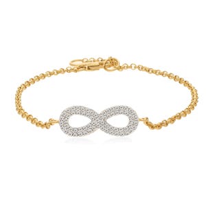 Puede incluir: Un brazalete de cadena dorada con un dije en forma de infinito. El dije está cubierto de pequeñas piedras transparentes.