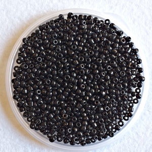 May include: A close-up image of a large quantity of small, black seed beads. The beads are round and have a smooth, shiny finish.