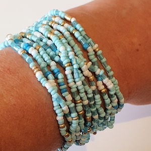 May include: A multi-strand bracelet made of blue, white, and gold beads. The bracelet is made of small, round beads and is layered to create a thick, textured look.