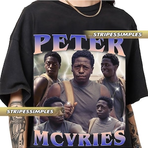 May include: Black t-shirt featuring a graphic of a man with the text "PETER MCVRIES" in a retro style. The design includes multiple images of the same person with a lightning bolt effect. The brand name "STRIPESSIMPLES" is also visible.