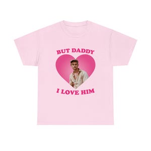 Puede incluir: Camiseta rosa claro con un corazón rosa. El texto "BUT DADDY I LOVE HIM" está encima y debajo del corazón. Dentro del corazón hay una foto de un hombre. La camiseta es de cuello redondo.