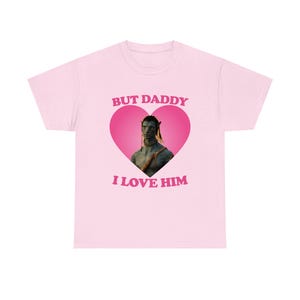 Puede incluir: Camiseta rosa claro con un gráfico de un personaje de la película Avatar dentro de un corazón rosa. El texto "BUT DADDY" está encima del corazón y "I LOVE HIM" debajo. La camiseta es de cuello redondo.