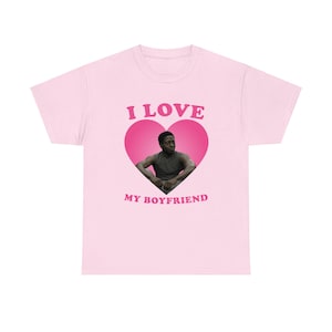 May include: Light pink t-shirt with a graphic that says "I LOVE MY BOYFRIEND" in pink text. The graphic features a pink heart with a photo of a man inside.