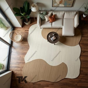 May include: An area rug with an irregular, organic shape featuring a large cream-colored central section contrasted by two rounded, tan-colored sections on opposite sides. The rug has a textured surface and is placed on a dark wood floor.