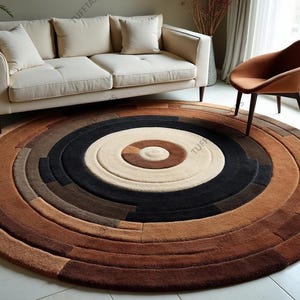 May include: A round rug with a concentric design in shades of brown, beige, and black. The rug features a circular pattern with varying textures and tones, creating a layered effect. The rug is placed on a tiled floor, with a cream-colored sofa and a brown chair in the background.