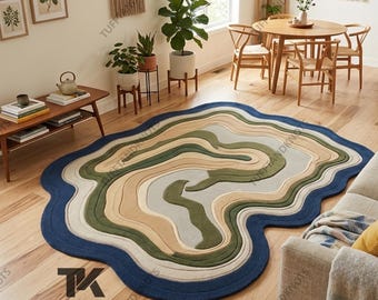 Puede incluir: Una alfombra abstracta grande con una forma ondulada y orgánica. La alfombra presenta un borde azul oscuro, con capas de tonos verdes, beige y grises en el centro. Está colocada sobre un suelo de madera en un salón.
