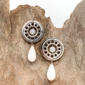 Könnte beinhalten: Ein Paar silberne Ohrringe mit einem runden Design und einem weißen tropfenförmigen Anhänger. Die Ohrringe sind aus Metall und haben ein rundes Design mit einem weißen tropfenförmigen Anhänger.