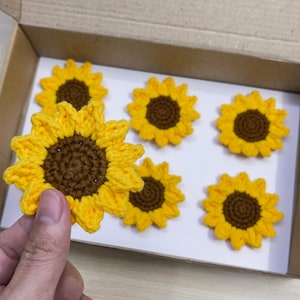 May include: Six crocheted sunflower embellishments in a box. The sunflowers are yellow with brown centers.