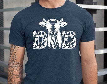 Könnte beinhalten: Ein marineblaues T-Shirt mit einer weißen Kuh, die eine Sonnenbrille trägt, und dem Wort "DAD" in einem Tarnmuster.