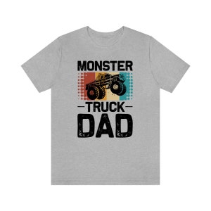 May include: A grey t-shirt with a vintage-style graphic of a monster truck. The text "Monster Truck Dad" is printed on the shirt.