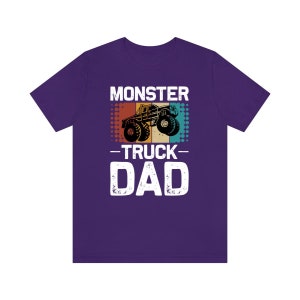 May include: Purple t-shirt with a vintage-style graphic of a monster truck and the text "Monster Truck Dad".