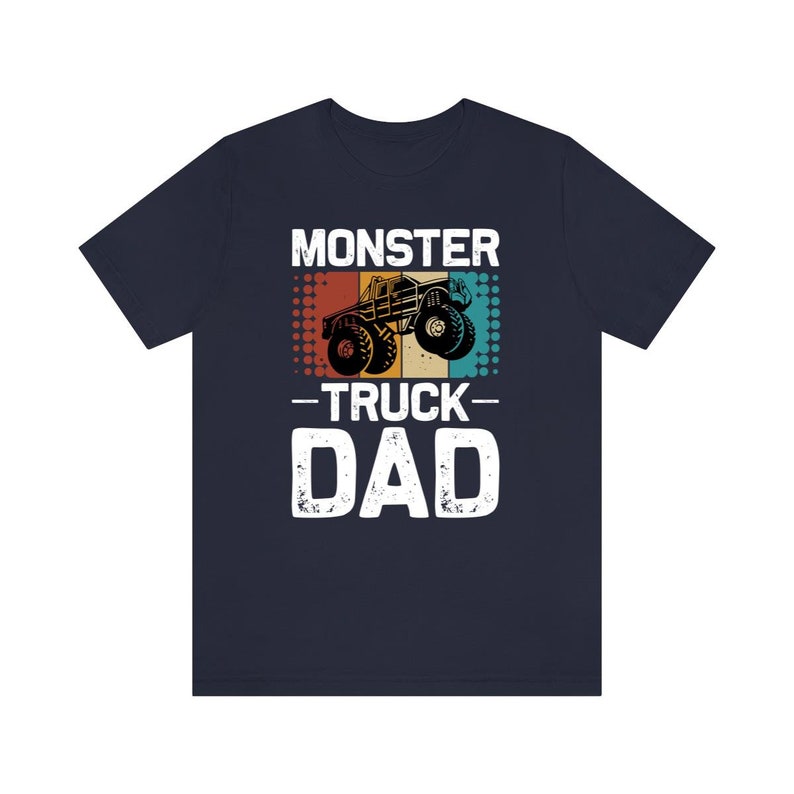 May include: A navy blue t-shirt with a vintage-style graphic of a monster truck. The text "Monster Truck Dad" is printed in white on the shirt.