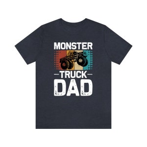 May include: A dark blue t-shirt with a vintage-style graphic of a monster truck. The text "Monster Truck Dad" is printed in white on the shirt.