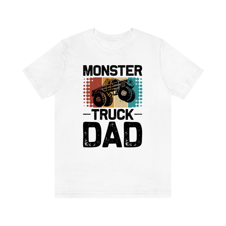 May include: White t-shirt with a vintage-style graphic of a monster truck. The graphic has a red, orange, and blue color scheme and the text "Monster Truck Dad".