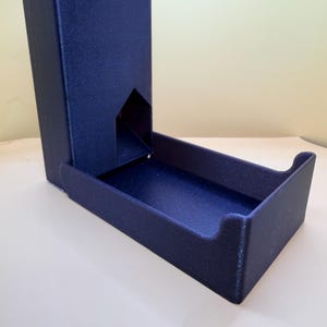 Op de afbeelding: Een donkerblauwe dobbelsteentoren met een glinsterende, getextureerde afwerking. De structuur heeft een hoge, verticale schacht met een vijfhoekige opening aan de basis die uitkomt in een rechthoekig bakje om rollende dobbelstenen op te vangen.