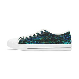 Op de afbeelding: Witte lage canvas sneakers met een zwarte rand rond de zool. De schoenen hebben een kleurrijk, iriserend patroon dat lijkt op een abalone-schelp.
