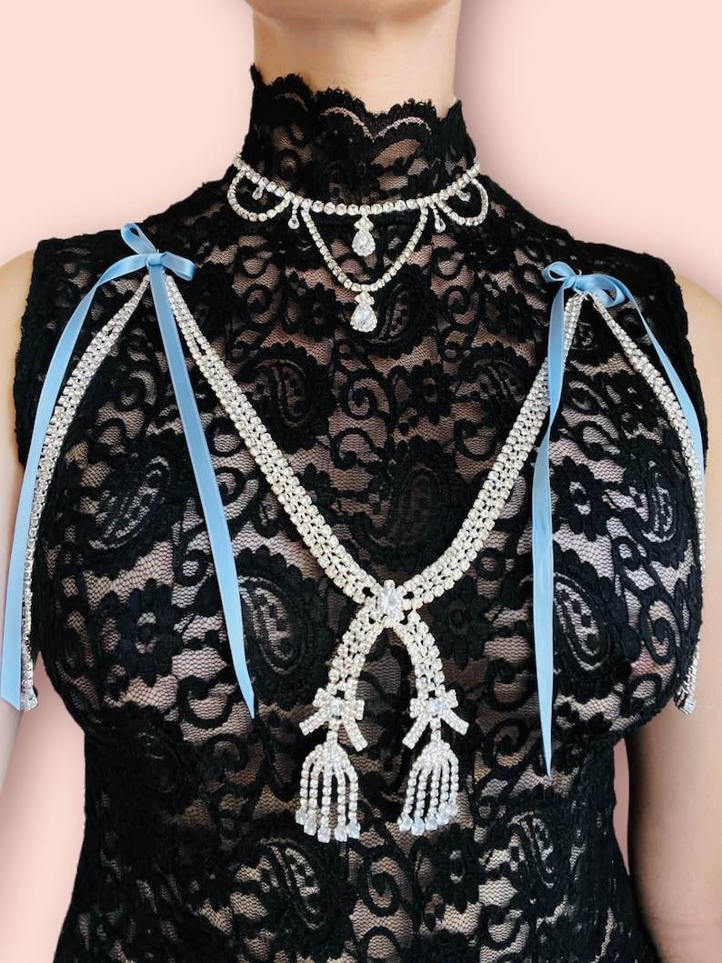May include: A black lace top with a rhinestone choker and a rhinestone necklace with two dangling tassels. The necklace has blue ribbon ties.