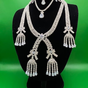 May include: A silver rhinestone necklace set with a choker, a longer necklace with a bow and tassel, and matching earrings with bows and tassels.