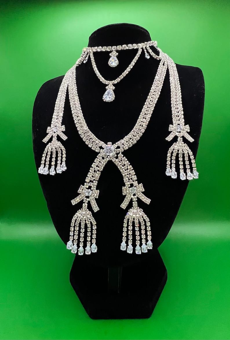May include: A silver rhinestone necklace set with a choker, a longer necklace with a bow and tassel, and matching earrings with bows and tassels.