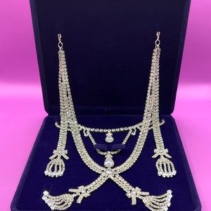 May include: A set of silver-toned rhinestone jewelry in a blue velvet box. The set includes a necklace, earrings, and a headpiece.