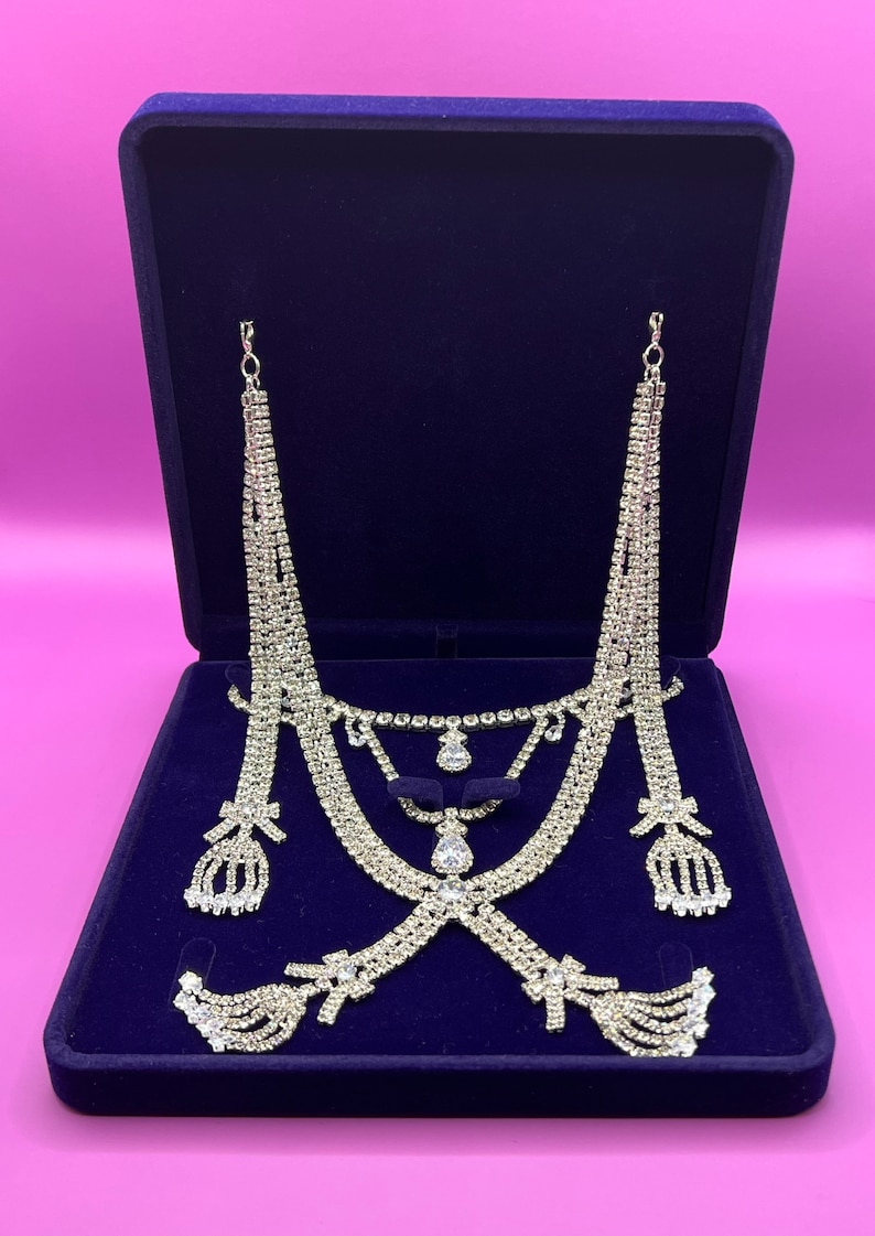 May include: A set of silver-toned rhinestone jewelry in a blue velvet box. The set includes a necklace, earrings, and a headpiece.