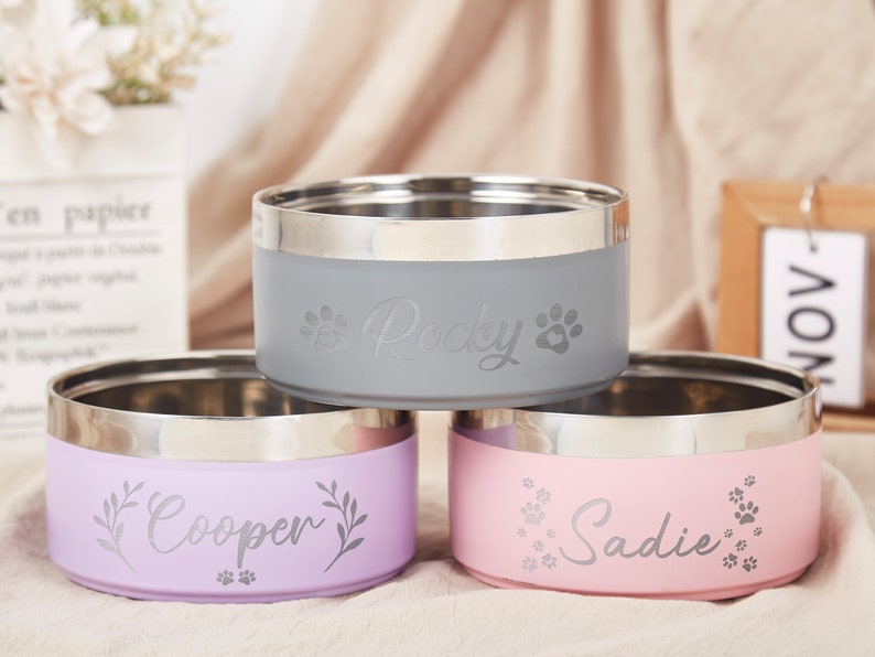 K&ouml;nnte beinhalten: Drei personalisierte Edelstahl-Napf f&uuml;r Haustiere. Die N&auml;pfe sind grau, lila und rosa. Die N&auml;pfe sind mit den Namen "Paddy", "Cooper" und "Sadie" graviert.