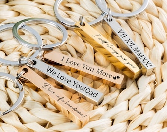 May include: Four gold and silver bar keychains with engraved messages. The messages are "I Love You More", "We Love You! Dad", "Drive safe handsome!" and "VII.XII.MMXXI I will always pick you!"