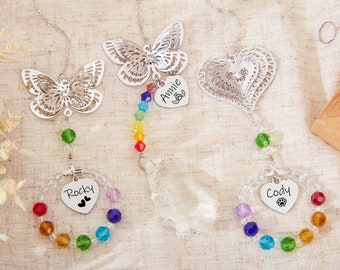 May include: Three silver wind chime ornaments with rainbow crystal beads. The ornaments feature a butterfly, a heart, and a heart with a paw print. The hearts are engraved with the names "Annie", "Rocky", and "Cody".