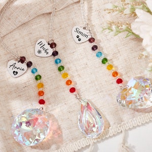 Puede incluir: Tres atrapasoles de cristal arco&iacute;ris con etiquetas personalizadas en forma de coraz&oacute;n. Las etiquetas dicen "Annie", "Malia" y "Simon".