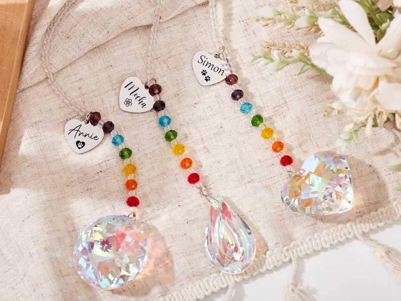 Puede incluir: Tres atrapasoles de cristal arco&iacute;ris con etiquetas personalizadas en forma de coraz&oacute;n. Las etiquetas dicen "Annie", "Malia" y "Simon".