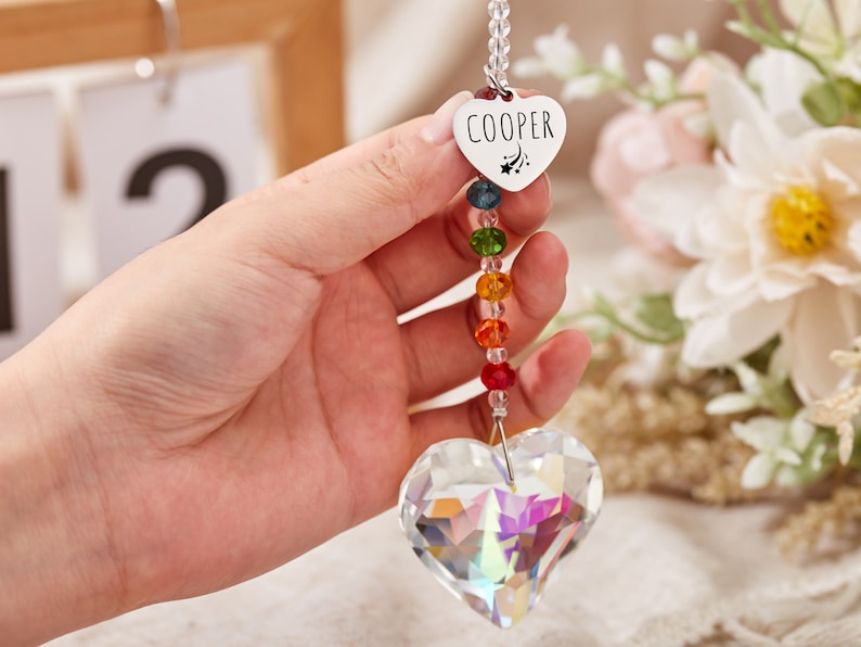 Puede incluir: Un atrapasol de cristal en forma de coraz&oacute;n con cuentas de arco&iacute;ris y un dije de coraz&oacute;n plateado con el nombre "COOPER" grabado.