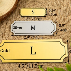 May include: Three metal nameplates in gold and silver, labeled S, M, and L. The gold nameplate labeled L measures 4.5 inches by 1.5 inches. The silver nameplate labeled M measures 2.9 inches by 0.9 inches. The gold nameplate labeled S measures 1.85 inches by 0.59 inches.