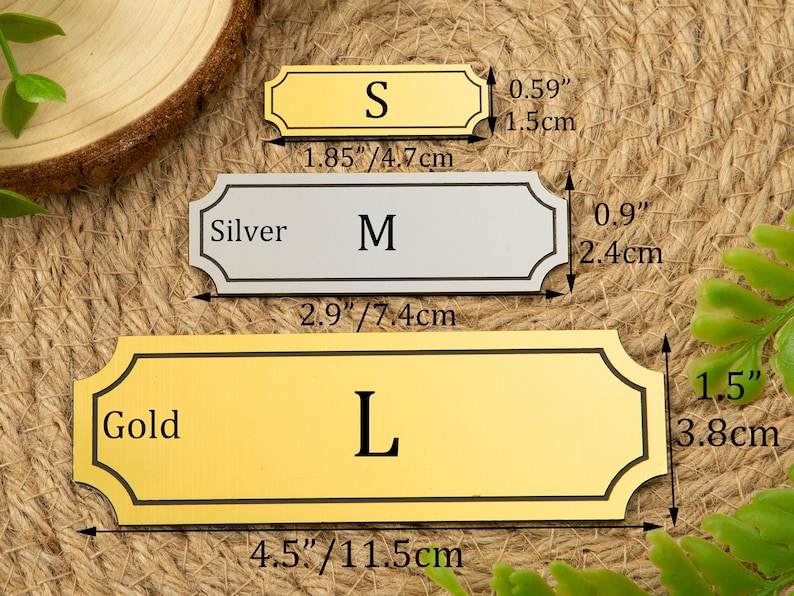May include: Three metal nameplates in gold and silver, labeled S, M, and L. The gold nameplate labeled L measures 4.5 inches by 1.5 inches. The silver nameplate labeled M measures 2.9 inches by 0.9 inches. The gold nameplate labeled S measures 1.85 inches by 0.59 inches.