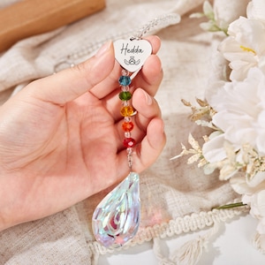 Puede incluir: Un atrapasol de cristal arco&iacute;ris con un dije en forma de coraz&oacute;n que dice "Hedda" y un cristal transparente en forma de l&aacute;grima en la parte inferior.