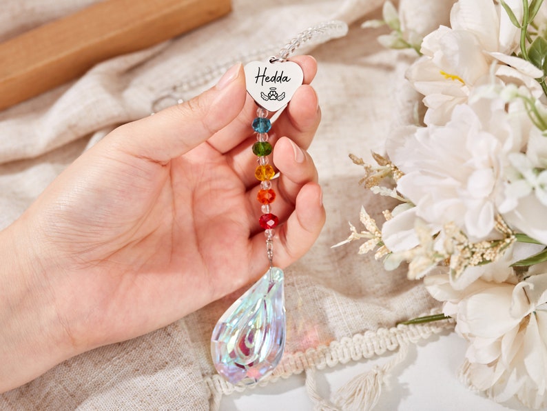 Puede incluir: Un atrapasol de cristal arco&iacute;ris con un dije en forma de coraz&oacute;n que dice "Hedda" y un cristal transparente en forma de l&aacute;grima en la parte inferior.