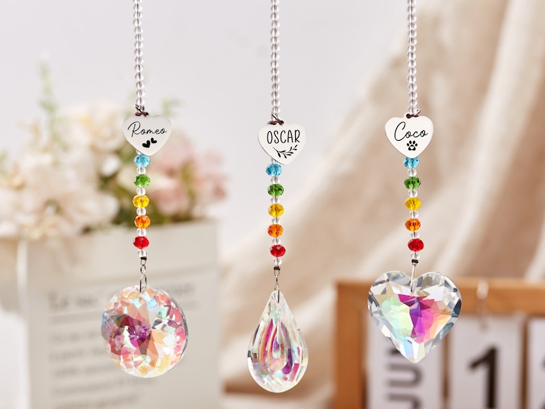 Puede incluir: Tres atrapasoles de cristal arco&iacute;ris con dijes personalizados en forma de coraz&oacute;n. Los dijes est&aacute;n grabados con los nombres "Romeo", "Oscar" y "Coco".