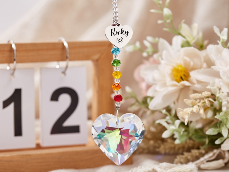 Puede incluir: Un atrapasol de cristal arco&iacute;ris con un cristal en forma de coraz&oacute;n en la parte inferior. El atrapasol tiene un dije de coraz&oacute;n plateado con la palabra "Rocky" y un peque&ntilde;o s&iacute;mbolo de sol grabado en &eacute;l.