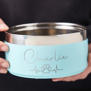 K&ouml;nnte beinhalten: Eine hellblaue Edelstahl-Hundenapf mit einem silbernen Pfotenabdruck und einem Herzschlag-Design. Die Sch&uuml;ssel ist mit dem Namen "Charlie" graviert.