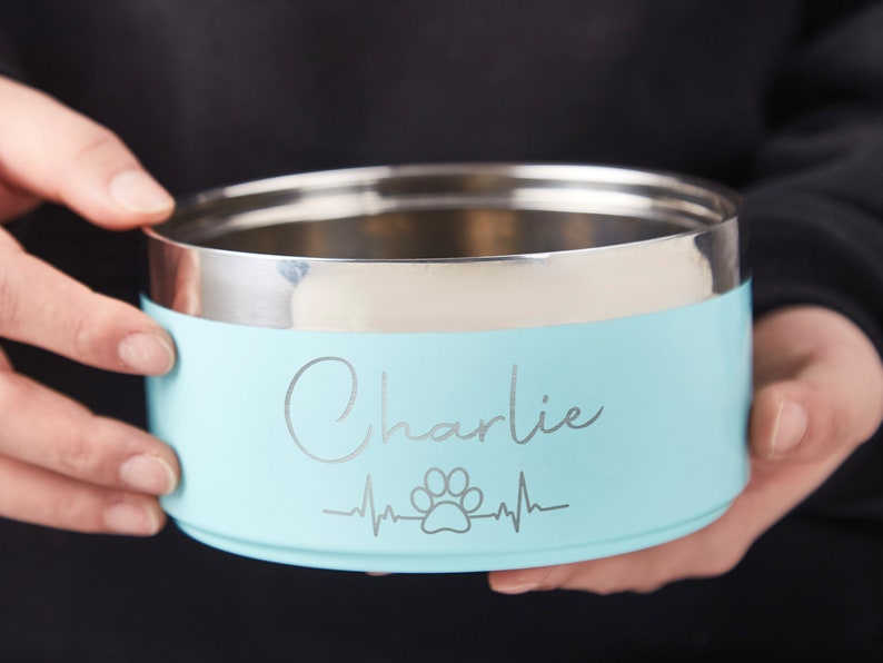 K&ouml;nnte beinhalten: Eine hellblaue Edelstahl-Hundenapf mit einem silbernen Pfotenabdruck und einem Herzschlag-Design. Die Sch&uuml;ssel ist mit dem Namen "Charlie" graviert.