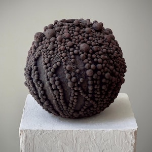 Dark earthy biomorphic vase with dense textured paper-clay spheres and raw organic surface.