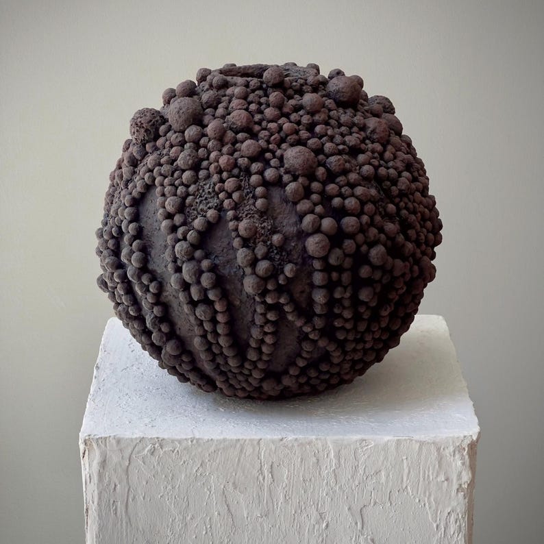 Dark earthy biomorphic vase with dense textured paper-clay spheres and raw organic surface.