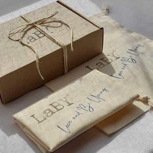 May include: A brown cardboard box tied with twine and labeled "Labr" is sitting on top of a white canvas bag with the text "Labr Love and Be Young" printed on it.