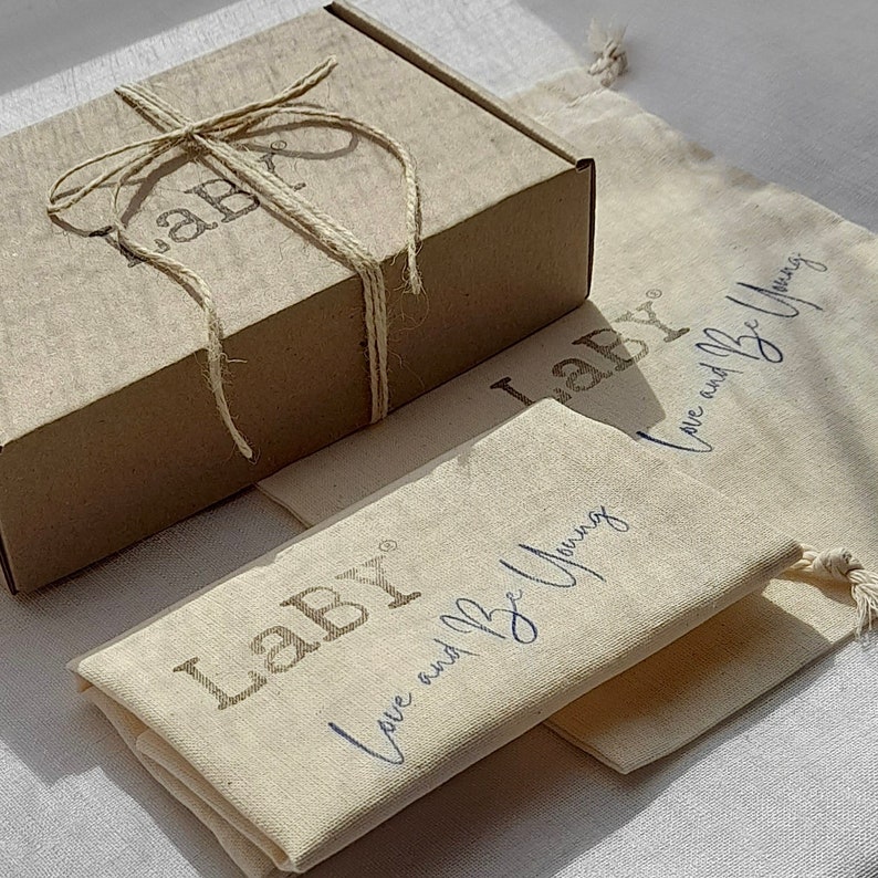May include: A brown cardboard box tied with twine and labeled "Labr" is sitting on top of a white canvas bag with the text "Labr Love and Be Young" printed on it.