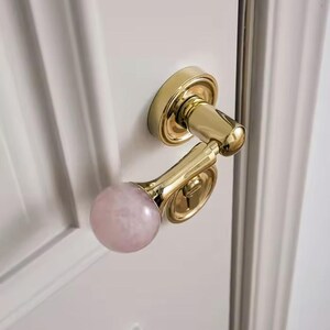 May include: A gold door handle with a pink, round knob. The handle is attached to a white door.