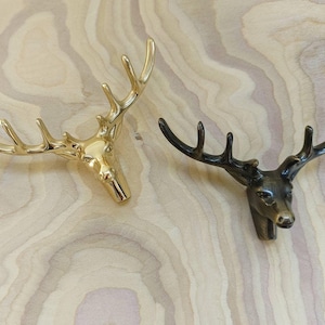 May include: Two decorative deer head sculptures. One is gold-coloured, the other is bronze. Both have detailed antlers and are mounted on a light wood surface. These sculptures are ideal for adding a rustic touch to home decor.