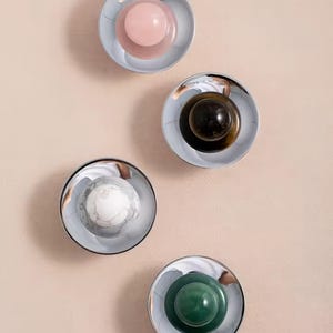 以下が含まれることがあります： 鏡面仕上げの装飾的な丸いオブジェクトが4つ。各オブジェクトには、ピンク、濃い茶色、白い大理石、緑色の中心的な色の球があります。オブジェクトは、明るいピンク色の背景に対して垂直に配置されています。